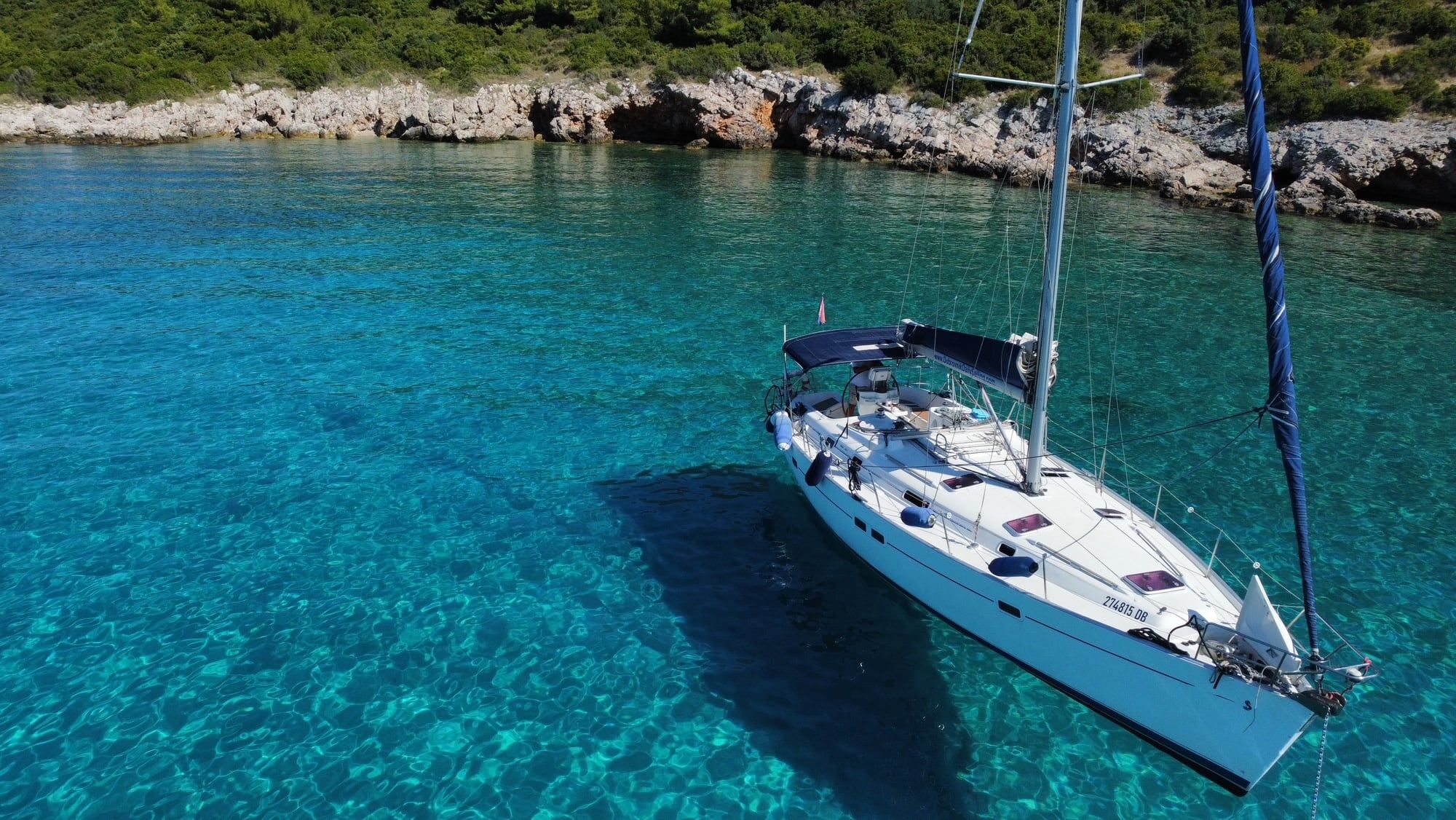 Sailing boat anchored in a turquoise bay, seen from above